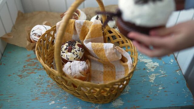 Female hands put Easter cakes creatively decorated with white icing, candied fruits, nuts and chocolate into authentic plaited basket. Stylish traditional Easter buns on linen tablecloth.