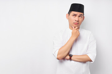Portrait of pensive young Asian Muslim man looking at empty space, touching his chin, thinking about offer isolated on white background. People religious Islamic lifestyle concept - Powered by Adobe