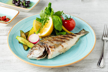 Grilled sea bream with vegetables and greens on wooden table