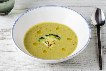 Healthy broccoli soup with a slice of grilled broccoli on a white porcelain plate