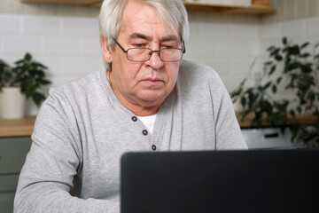 Senior male business owner in glasses sitting at desk in front of laptop. Successful older male...