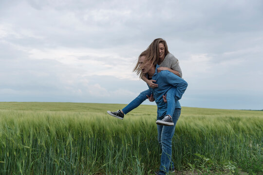 Young man piggybacking woman on grassy field against cloudy sky