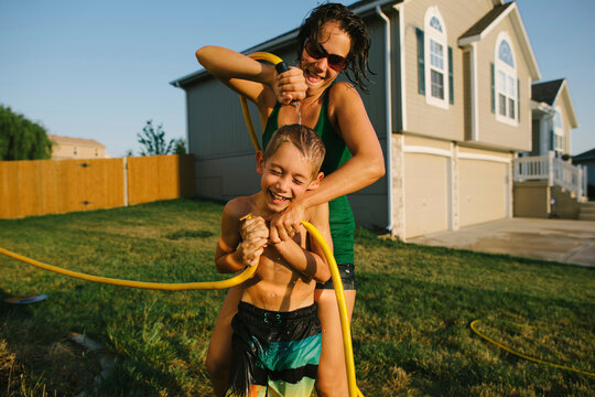 Happy son getting wet by mother with hose pipe in yard