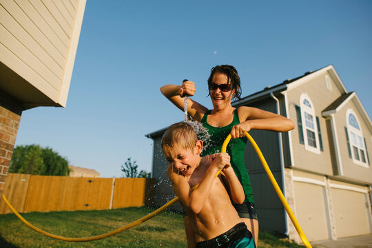 Playful mother pouring water on son using hose pipe in yard