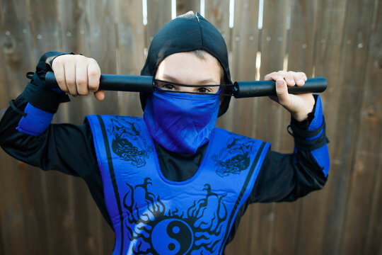 Portrait of boy in ninja costume standing against wooden fence
