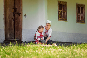 Fototapeta na wymiar mother and daughter in traditional Ukrainian clothes are sitting near the house