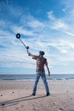 Rear view of man holding recreational metal detector at Horsey Beach