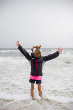 Playful girl in horse mask playing at beach against clear sky