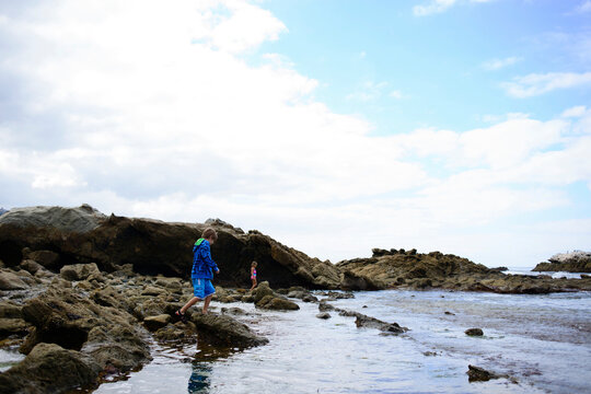 Side view of brother and sister walking on rocks at Laguna Beach