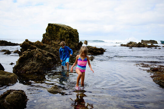 Brother and sister walking in water by rocks at Laguna Beach