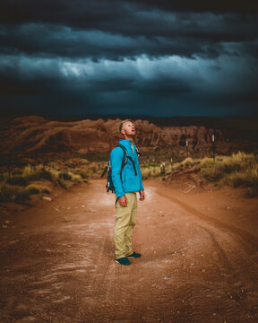 Full length of hiker standing on dirt road against storm clouds