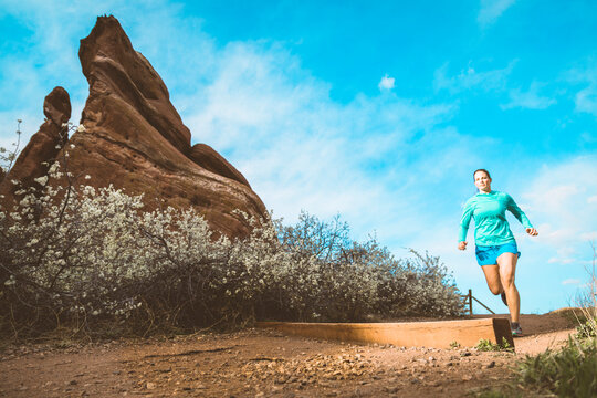 Determined sportswoman jogging on dirt trail by rock formation against sky