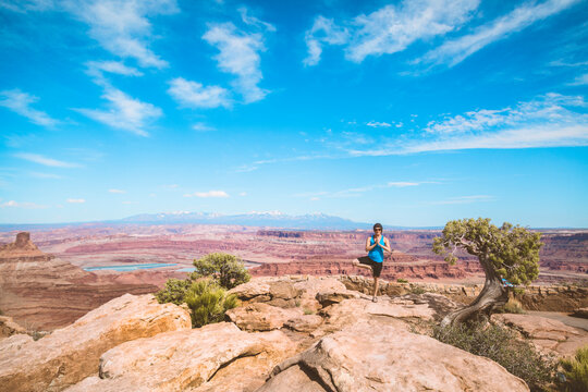 Mature woman performing yoga in tree pose on mountain against blue sky