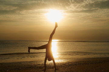 Silhouette girl doing handstand at beach against sky during sunset
