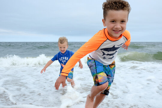 Carefree brothers playing on shore at beach against sky
