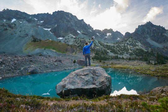 Rear view of hiker holding cap while standing on rock by lake against mountains at Olympic National Park