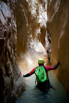 Rear view of hiker with backpack wading amidst canyon while canyoneering