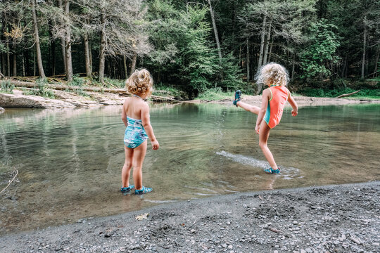Rear view of girl looking at sister kicking water while standing in lake