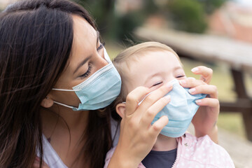 Mother and little girl using protective facial mask outdoors