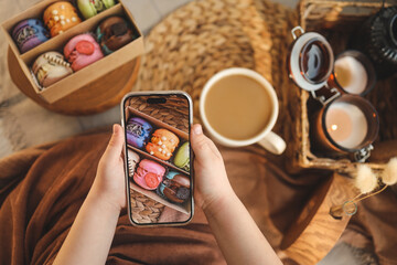 Girl taking a top-down photo of macaron box with various assortment using her phone