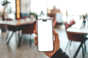 Girl holding phone with blank screen against blurred interior of cafe or restaurant. The background...