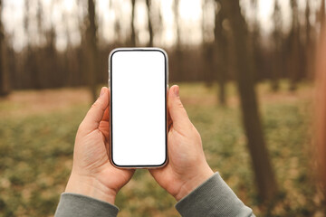 Hand holding phone with blank screen taking photo or selfie in the forest. There is no signal. The...