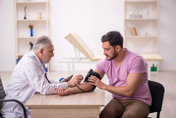 Old male doctor measuring young patient's blood pressure