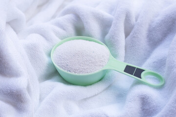 Detergent powder in measuring spoon on cloth before washing. Laundry concept.