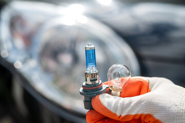 A man in a glove is holding a halogen high beam lamp near a car headlight close-up.