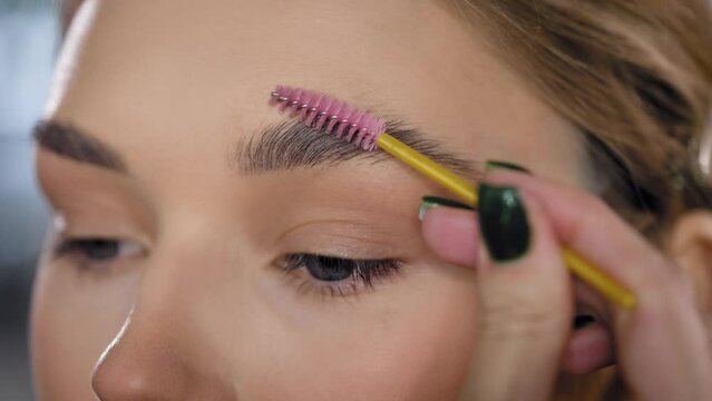 Close-up. Make-up artist combs and styles the eyebrows of a young blonde woman