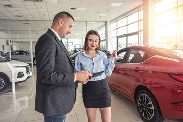 Fototapeta na wymiar Young girl sales consultant with a clipboard who advises a male client in a car dealership.