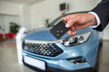 key in male hand against new modern car at showroom, success sale or rent deal
