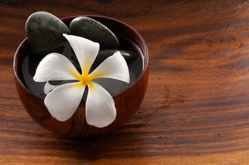 Fototapeta na wymiar Frangipani flowers and spa stones in wooden bowl 