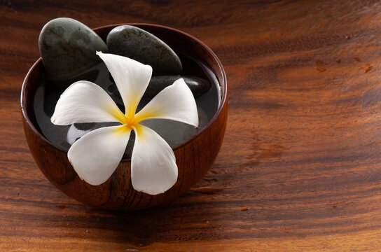 Frangipani flowers and spa stones in wooden bowl 