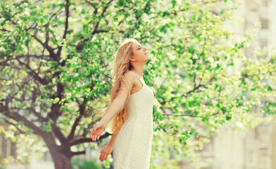 Fototapeta na wymiar Beautiful blonde young woman enjoying smell in spring blooming garden