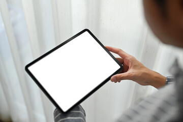 Close up view of man hand holding holding digital tablet while sitting in living room. White screen for webpage or advertise text