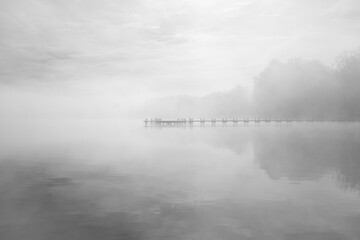 Fototapeta premium Jetty at the lake in the fog. Misty landscape in the morning. Idyllic nature by the water. Rest and relaxation. 