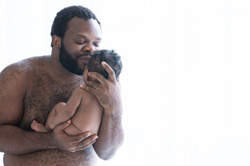 African American bearded father holding his cute newborn baby in his arms, Dad standing and kissing at baby forehead, infant boy 2 months old, Family and newborn care. White background, side view