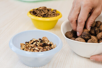Closeup photo of unrecognizable man taking out walnuts from bowl in kitchen