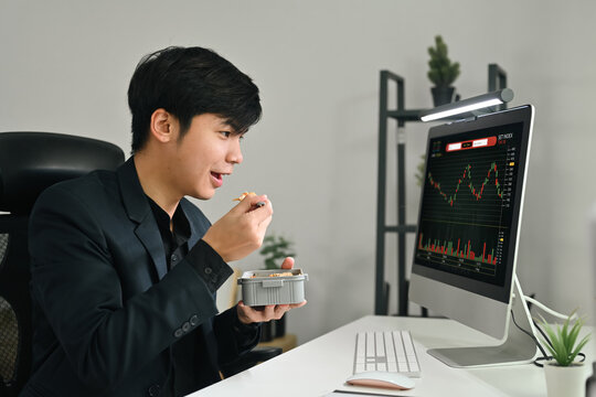 Young businessman or trader sitting at his office in front of computer screen and enjoying lunch break