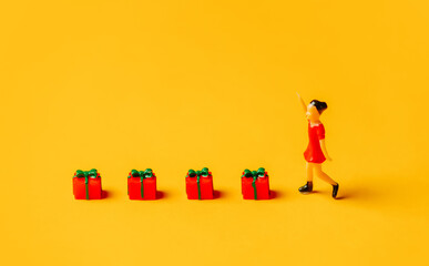 miniature girl figure next to red Christmas gift boxes on yellow background