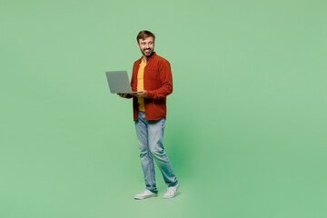 Full body side view elderly IT man 40s years old wears casual clothes red shirt t-shirt hold use work on laptop pc computer look aside isolated on plain pastel light green background studio portrait.