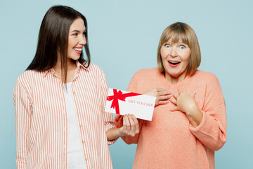 Surprised fun elder parent mom with young adult daughter two women together wears casual clothes hold store gift certificate coupon voucher card isolated on plain blue background. Family day concept.