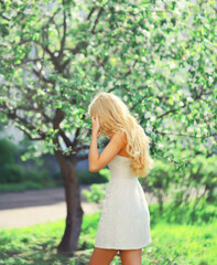 Plakat Beautiful blonde young woman in spring blooming garden on flowers tree background