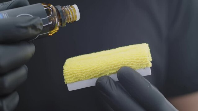 Close-up professional in black gloves applying a ceramic coating to the paintwork on a yellow sponge before work. Car wash concept