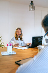 Smiling young blonde woman with headset in customer help service of coworking. Assistance and support help concept.