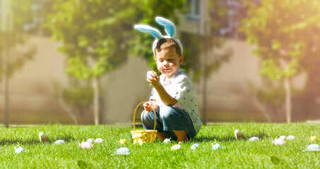 A boy collects Easter eggs on a green lawn, a sunny day. Easter photography, a wicker basket with colorful decorative eggs on a green lawn. A child plays in the yard. Easter Concept