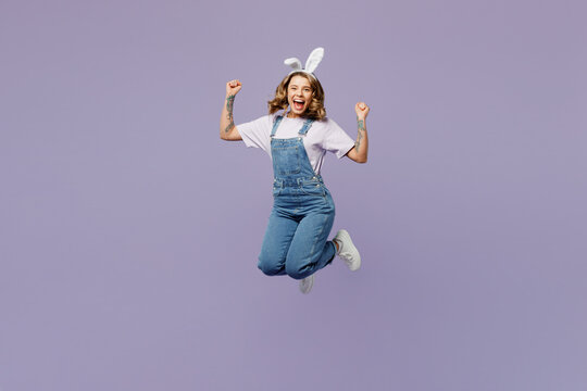 Full body overjoyed young woman wearing casual clothes bunny rabbit ears jump high do winner gesture isolated on plain pastel light purple background studio portrait. Lifestyle Happy Easter concept.