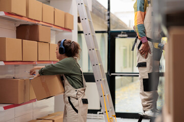 Worker looking at cardboard boxes in storage room, listening music at headphones while preparing customer orders in warehouse. Caucasian employee working at products delivery in storehouse