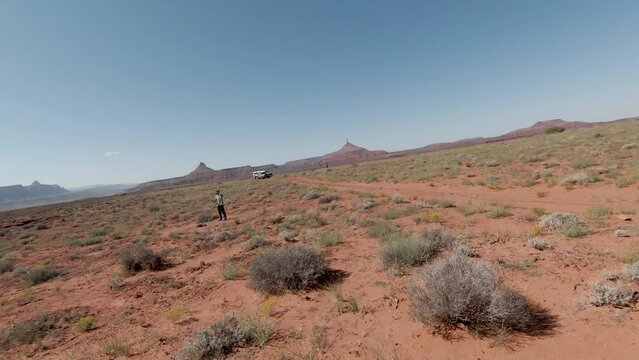 The guy has a helmet on his head and he controls a drone in middle of desert and cliffs in Indian Creek with sunny day.